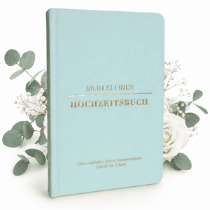 Das hellblaue "Mein kleines Hochzeitsbuch - Zarter Traum" von Mein kleines Hochzeitsbüro steht aufrecht als charmanter Hochzeitsplaner, geschmückt mit Eukalyptusblättern, weißen Rosen und Schleierkrautblüten.