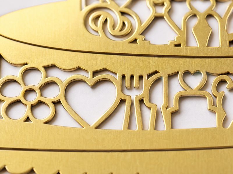 Nahaufnahme eines dekorativen goldenen Metallausschnitts mit den Formen einer Blume, eines Herzens, einer Gabel, eines Messers, eines Löffels und eines Tisches mit Stühlen, alles auf weißem Hintergrund.
