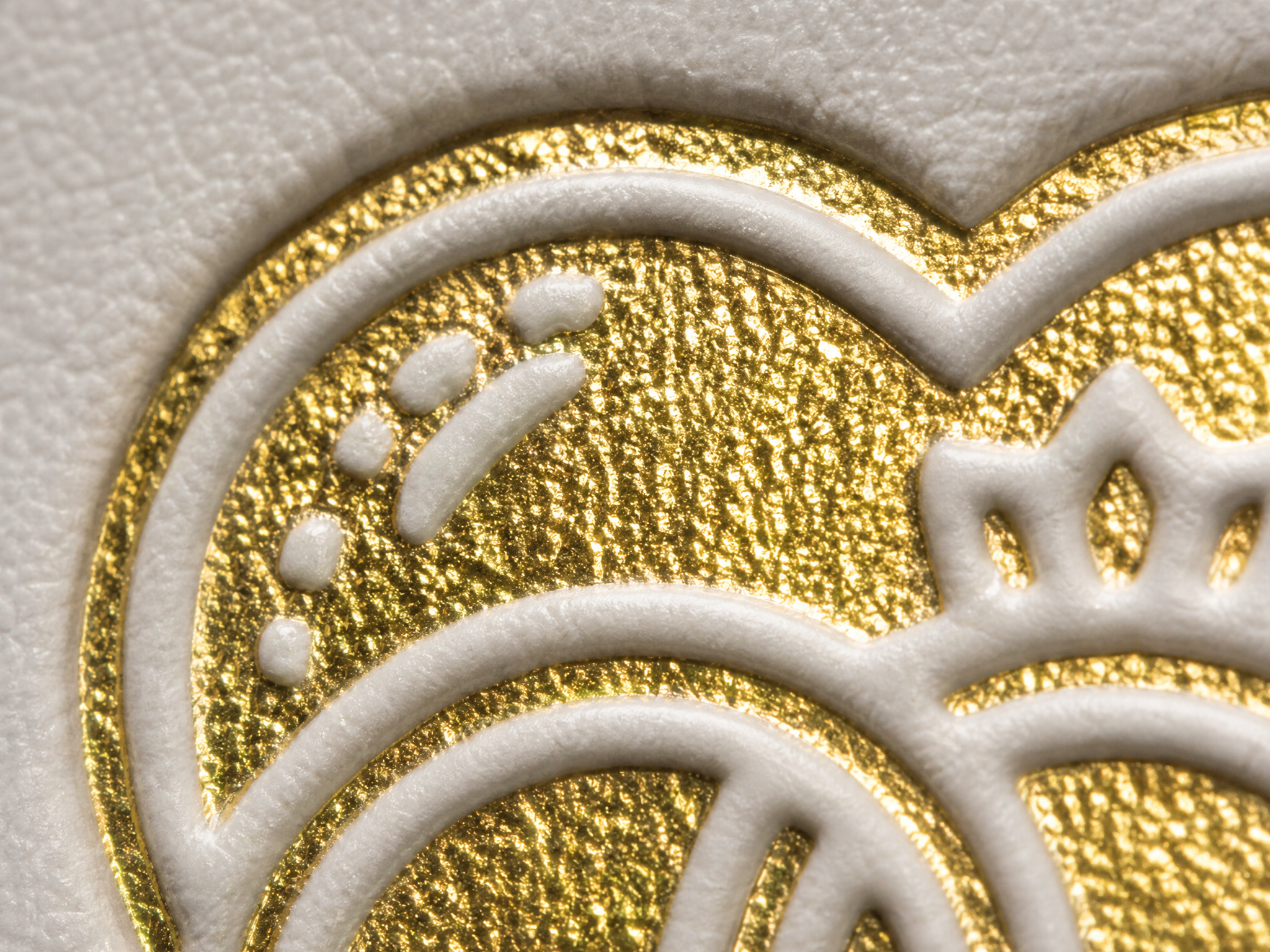 Nahaufnahme eines strukturierten, geprägten Goldfoliendesigns auf weißem Papier mit verschlungenen Linien und Punkten, die eine partielle Herzform und dekorative Muster bilden.