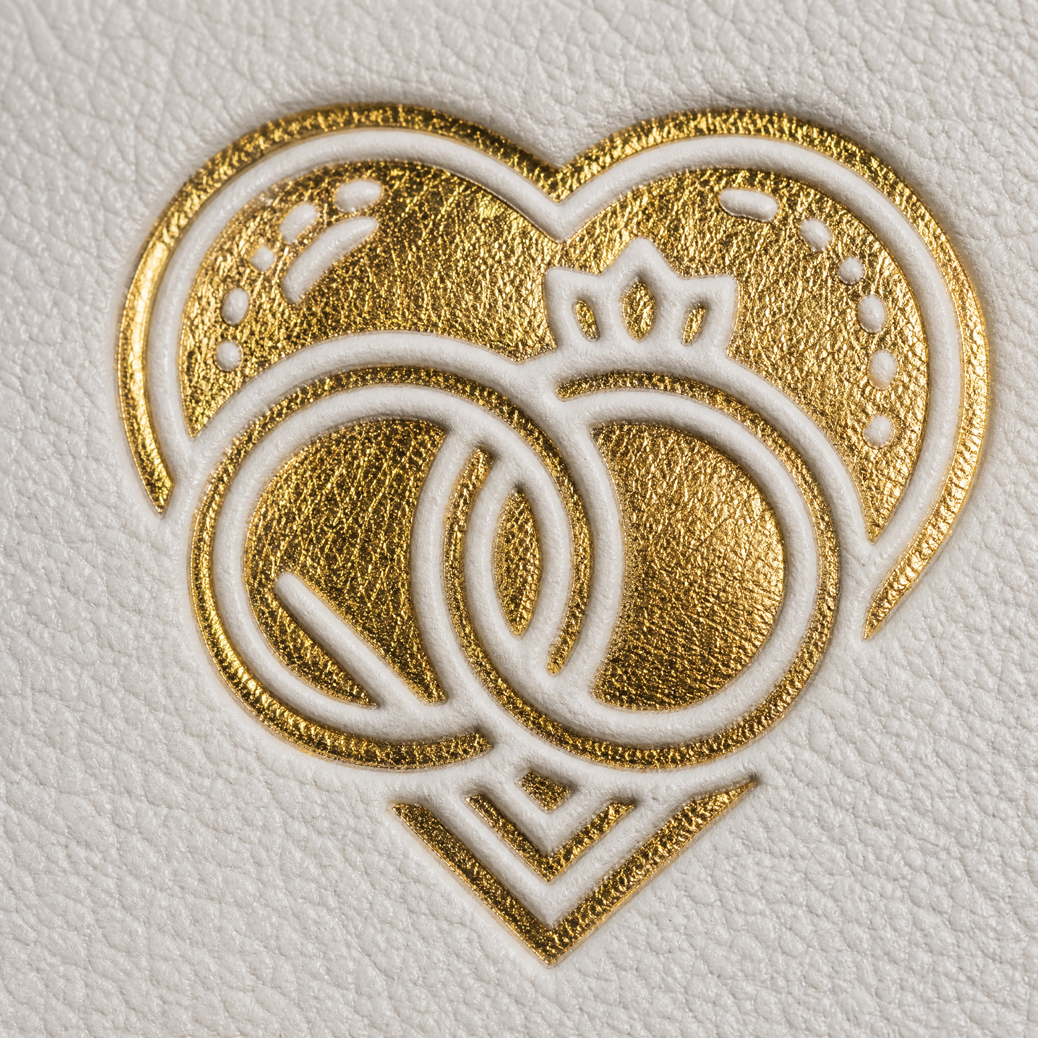 Goldgeprägtes Design auf strukturierter weißer Oberfläche mit zwei ineinander greifenden Ringen unter einem Herzumriss, die Liebe, Ehe oder Partnerschaft symbolisieren.