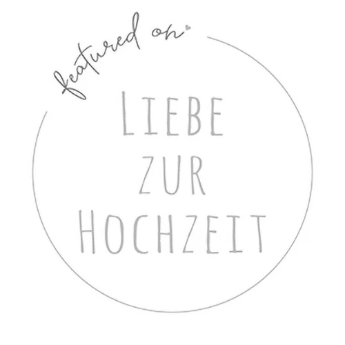 Ein weißes, kreisförmiges Abzeichen mit den handgeschriebenen Worten "featured on" oben und "Liebe zur Hochzeit" in der Mitte, geschrieben in Großbuchstaben mit einer minimalistischen, hellgrauen Schrift.