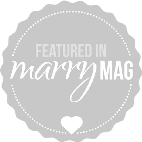 Ein rundes Abzeichen mit Wellenrand und gepunktetem Rand trägt die Aufschrift Featured in marry MAG in gemischten Schriftarten, mit einem kleinen Herz in der unteren Mitte. Das Design ist hellgrau und weiß.