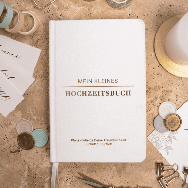 Das "Mein kleines Hochzeitsbuch - Ewige Eleganz" von Mein kleines Hochzeitsbüro ist ein weißer Samt-Hochzeitsplaner, der sich perfekt als Planungsbegleiter eignet und durch stilvolle Details wie Wachssiegel, Bänder und Papierausschnitte wunderbar ergänzt wird.