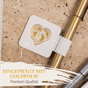 Der Stiftehalter - Schlaufe Extragroß von Mein kleines Hochzeitsbüro ist quadratisch, weiß und ziert zwei goldgeprägte Herzen. Befestigt an einem goldenen Stift auf beigem Steinsockel - Premium-Qualität für die Hochzeit.